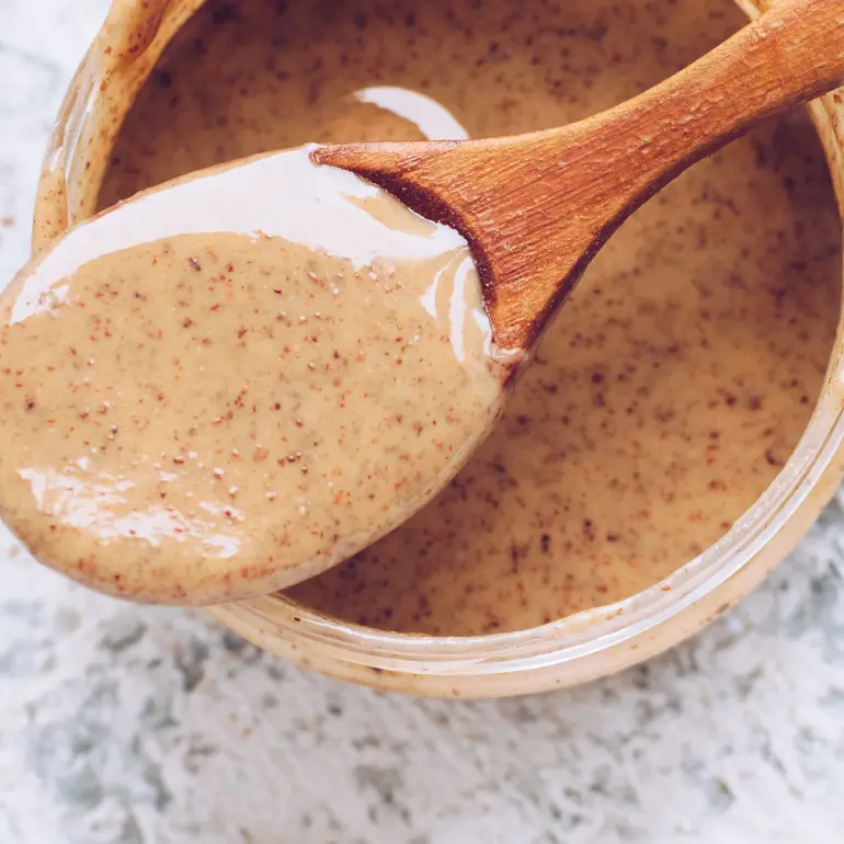 A wooden spoon scooping up natural almond butter from a bowl.