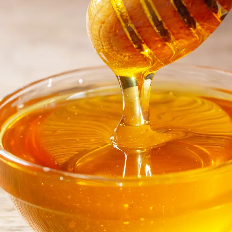 A honey wand dripping golden honey into a glass bowl.
