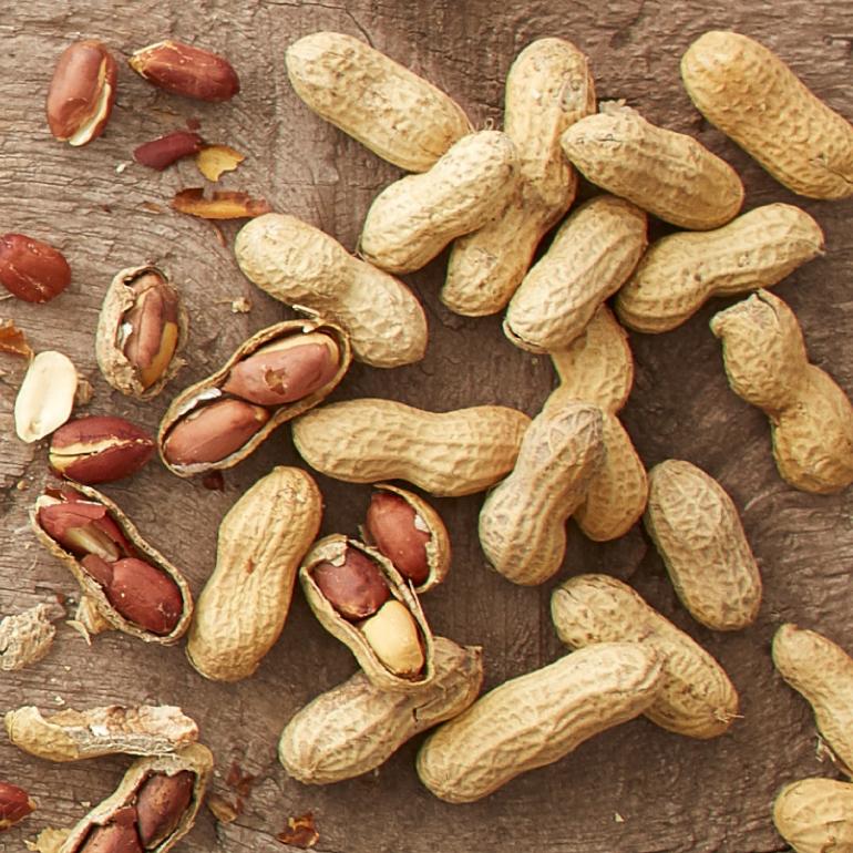 Whole peanuts in their shells are scattered on a table. Some have cracked open to reveal the peanuts inside.