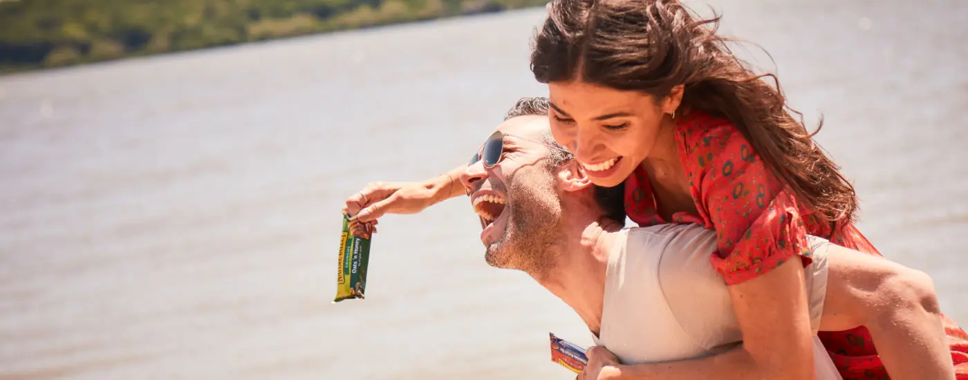 A man giving a woman a piggyback ride while she holds a Nature Valley bar in the wrapper.