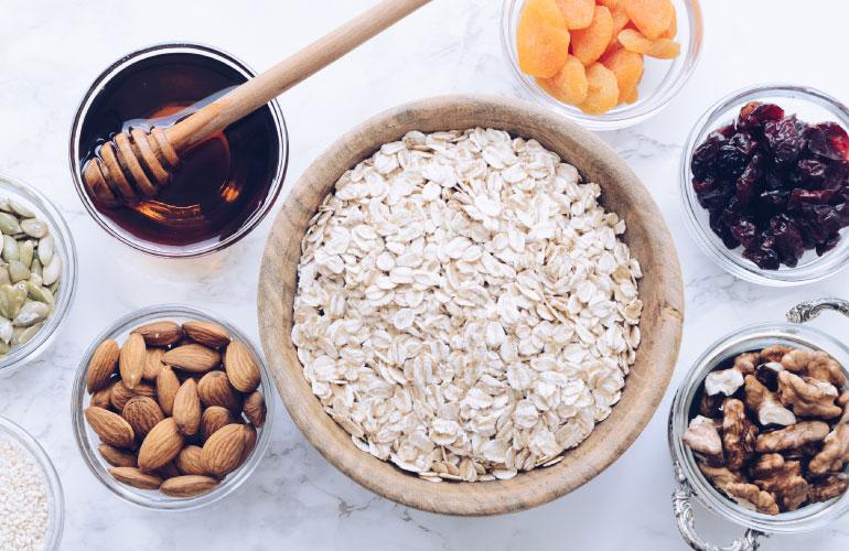 A dozen small glass bowls sitting on a marble countertop. The bowls contain fresh ingredients and dried fruits.