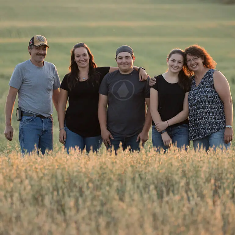 A smiling regenerative agriculture farm family posing proudly in their oat field.