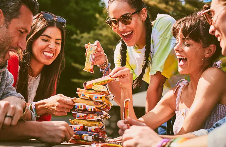 A group of people laughing around a stack of Nature Valley protein bars.