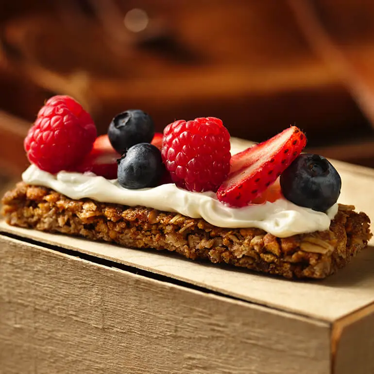 A Nature Valley Oats 'N Honey Crunchy Granola Bar spread with cream cheese and topped with fresh berries.