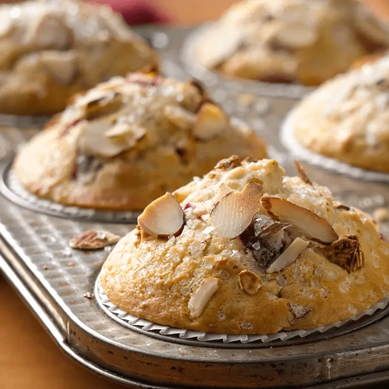 Muffins made with Nature Valley Cranberry Almond Protein Granola and cranberries topped with almond slices and granulated sugar in a muffin tin.