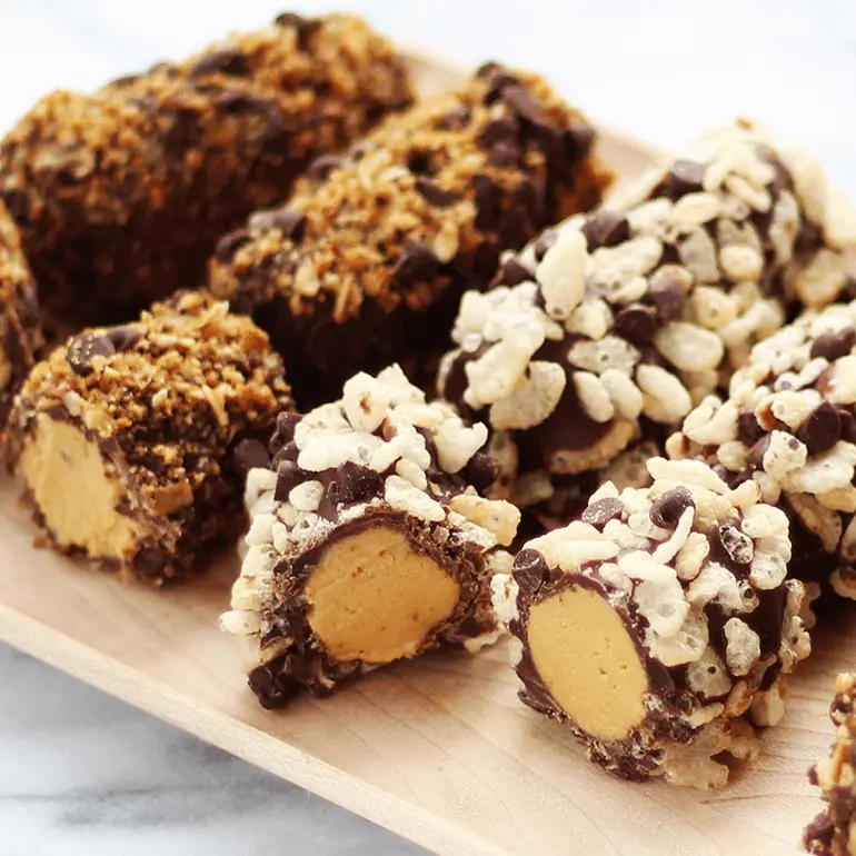 Boppers coated with with Nature Valley Oats 'N Honey Crunchy Granola Bars cut at the ends to show the peanut butter filling, served on a wood board.