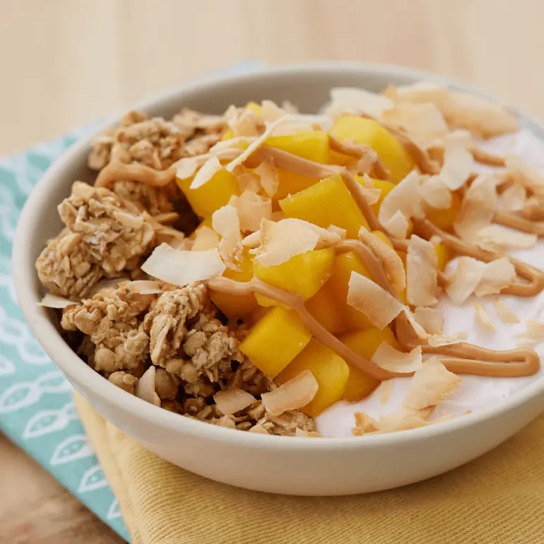 Strawberry banana yogurt bowl topped with Nature Valley Oats 'N Honey Protein Granola, mango, almond butter, and coconut flakes. Served in a bowl.
