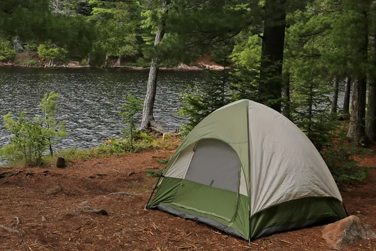 Picturesque wooded campsite with pitched tent next to a body of water.