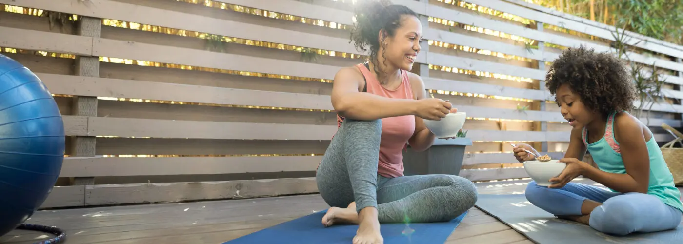Mother and daughter eating bowls of Nature Valley granola while sitting on yoga mats.