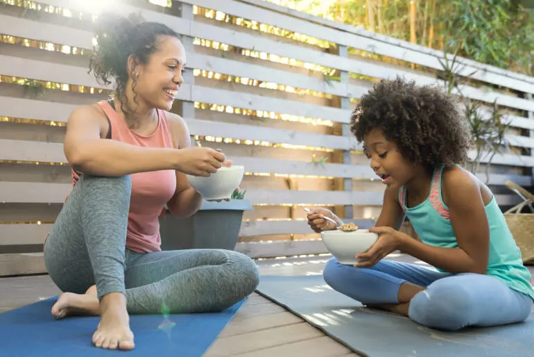 Mother and daughter eating bowls of Nature Valley granola while sitting on yoga mats.