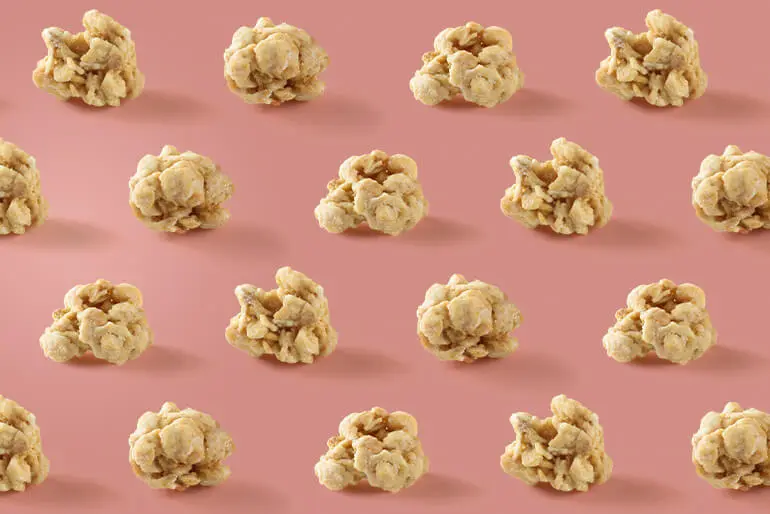 Rows of caramel popcorn clusters arranged neatly on a pink background.